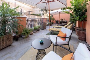 A patio area with outdoor furniture, including a round table and chairs, surrounded by potted plants and a railing. - Umiltà 36 - Preferred Hotels & Resorts (Rome)