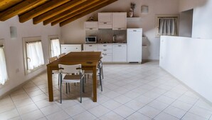 A dining area with a wooden table and chairs, a kitchen with white cabinets, and a sloped ceiling. - Appartamento "Orchidea", Agriturismo dai Gobbi (Fara Vicentino)