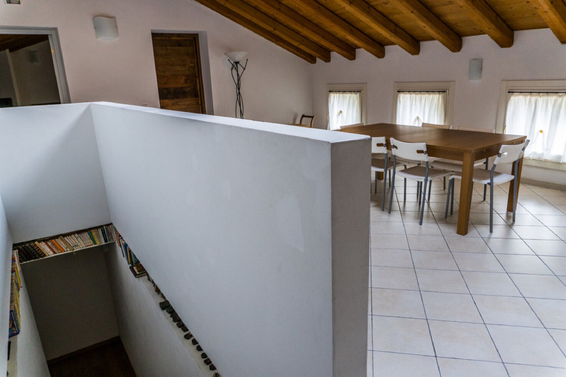 A dining area with a wooden table and chairs, a white partition, and a tiled floor.