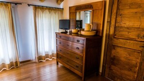A room with wooden flooring, a wooden dresser with drawers, a mirror, a television, and a door with a wooden panel. - Appartamento "Orchidea", Agriturismo dai Gobbi (Fara Vicentino)