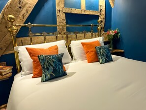 A bed with white bedding and two pillows, one orange and one with a leaf pattern, in a room with blue walls and a wooden ceiling. - Three Cocks Hotel (Brecon)