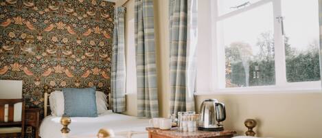 A bedroom with two beds, a wooden nightstand, a kettle, and a window with curtains.