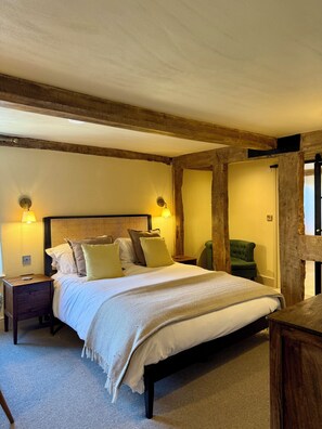 A bedroom with a bed, nightstands, a chair, and exposed wooden beams. - Three Cocks Hotel (Brecon)