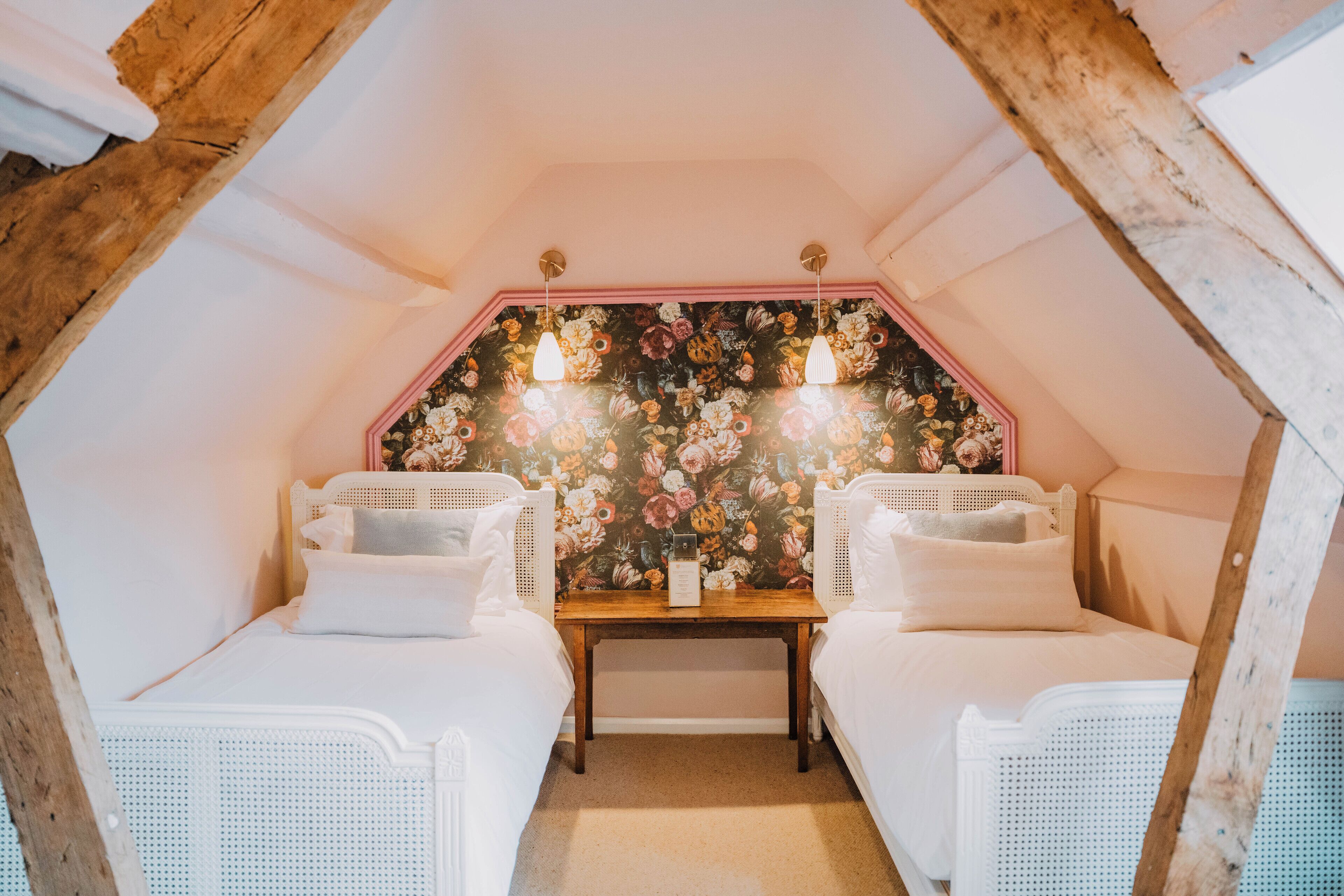 Un dormitorio ático acogedor con dos camas de mimbre blanco, papel tapiz floral y techo de madera.
