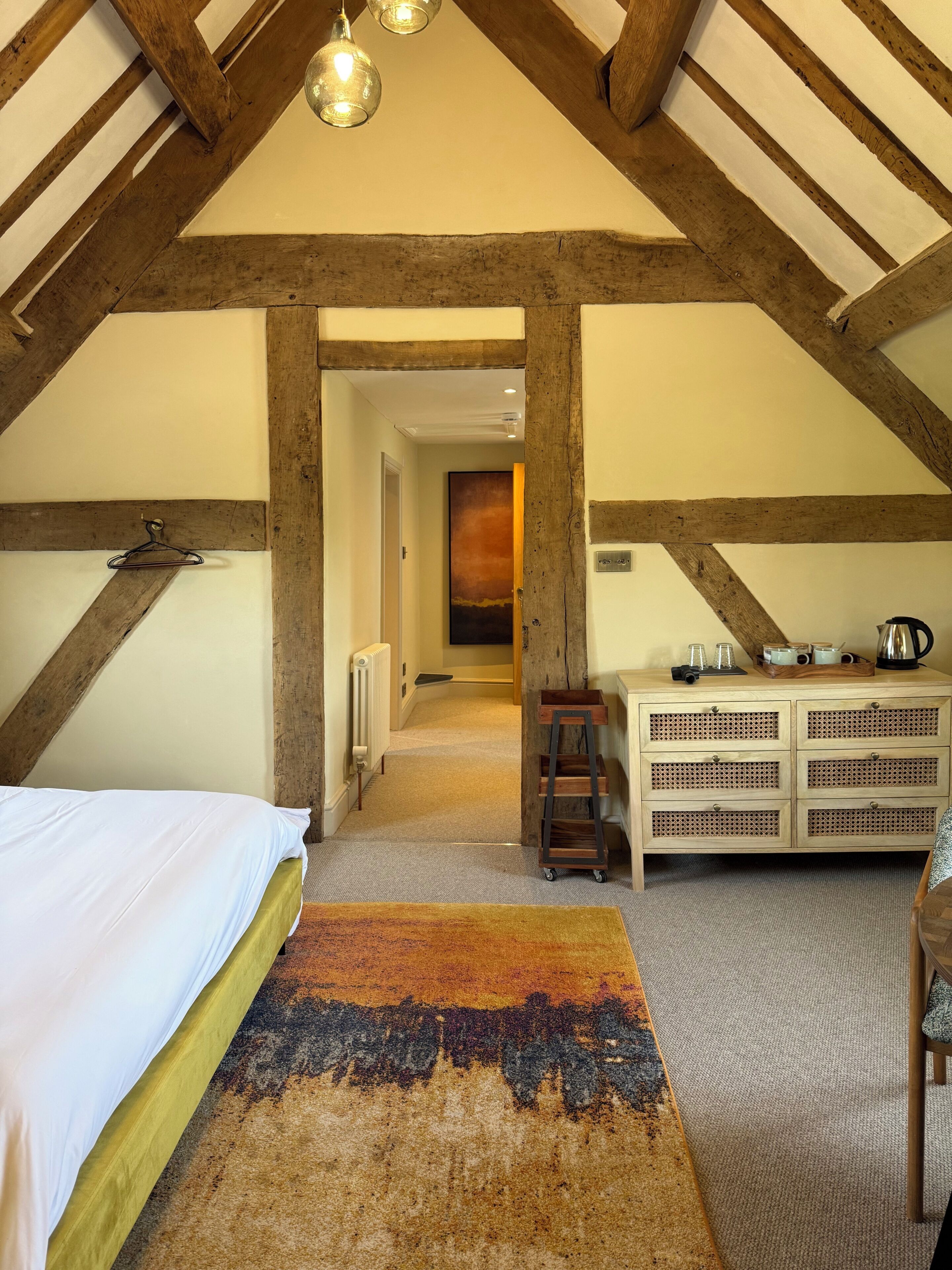 Un dormitorio con cama, cómoda de madera, lámpara colgante y un pasillo que lleva a otra habitación.