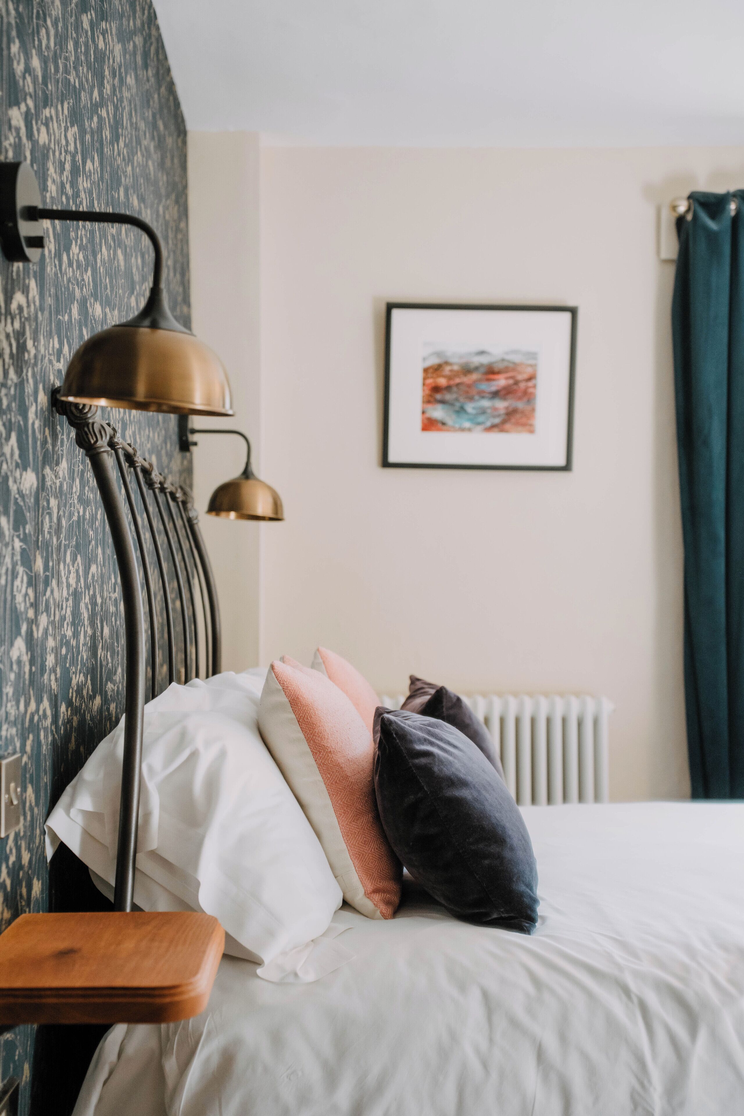 Un letto rifatto con cuscini, un comodino, una lampada e un quadro appeso al muro.