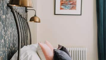 A neatly made bed with pillows, a bedside table, a lamp, and a framed picture on the wall.