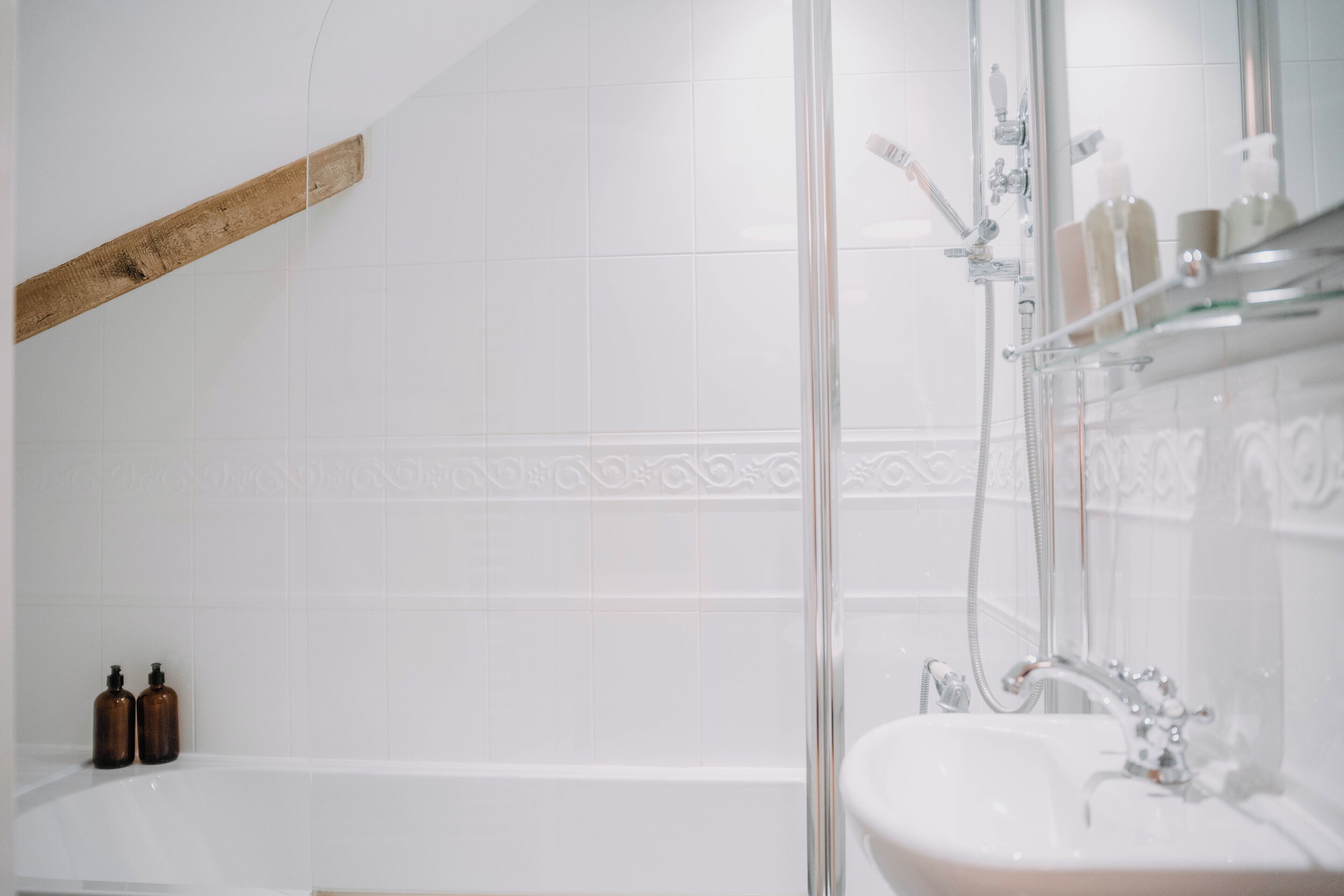 A bathroom with a bathtub, a shower, and a sink. There are two brown bottles on the edge of the bathtub.