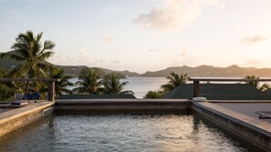 Una piscina con vistas al mar y a las montañas, rodeada de palmeras y una terraza de madera.