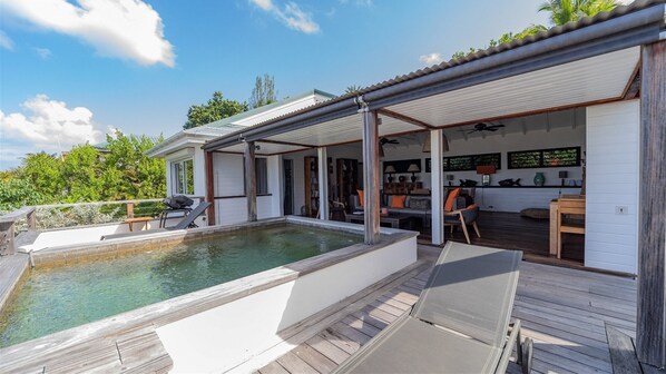 Zona de piscina con área de estar techada, piscina y vistas de la vegetación circundante.