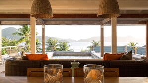 Un balcon agrémenté de lampes en osier, un canapé avec des coussins orange et une vue sur la mer et les montagnes.