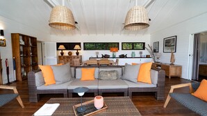Un salon chaleureux avec un canapé gris, des coussins orange et des lampes en osier.