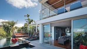 A modern two-story house with a glass balcony, a pool, and outdoor furniture.