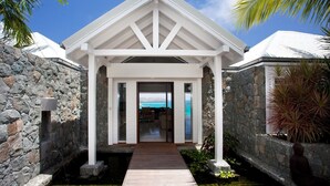 A modern building with a stone exterior, a wooden pathway leading to a covered entrance, and a view of the ocean. - Panama (3/5 Rooms) Luxury villa (Saint Jean)