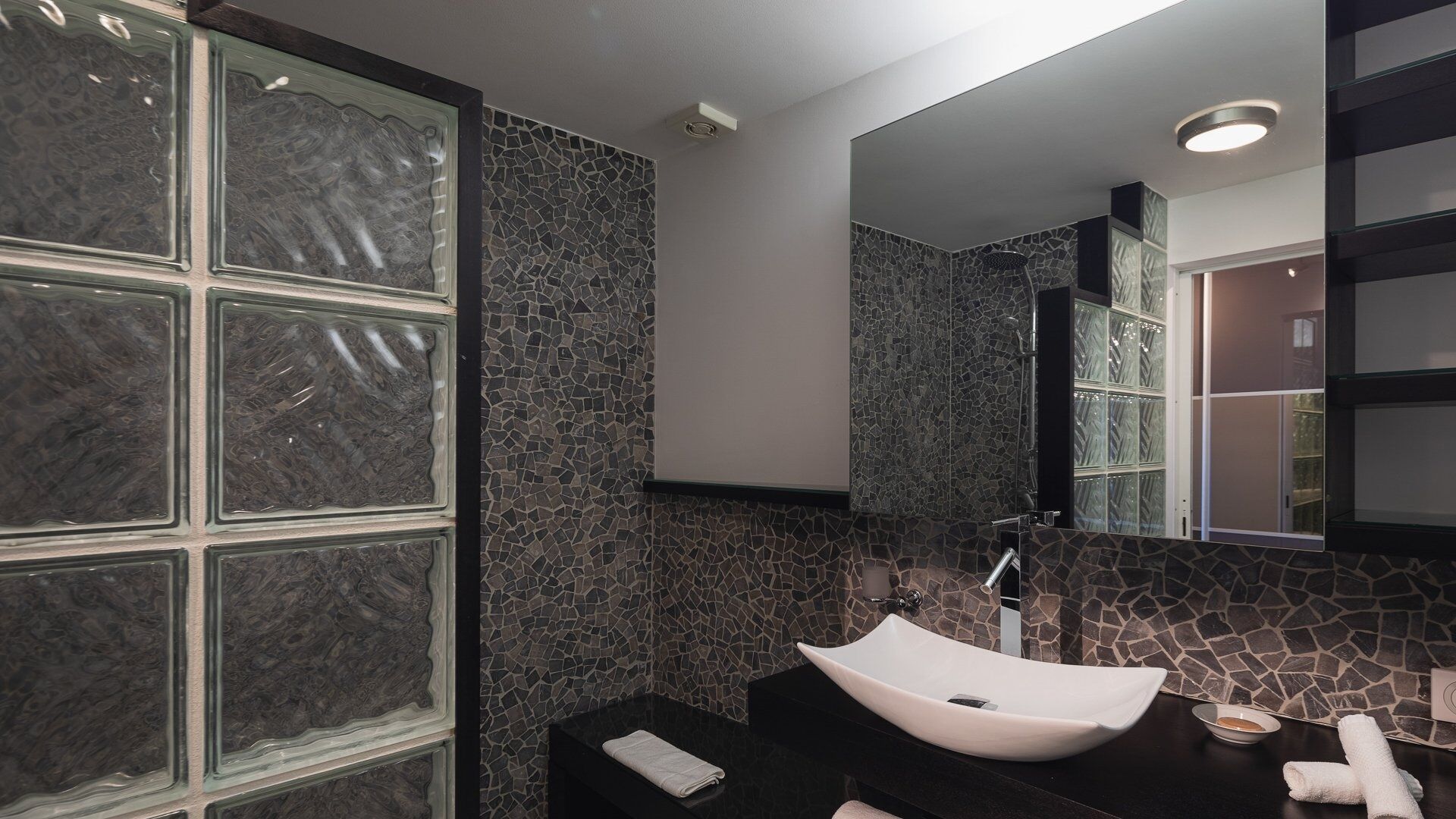 A bathroom with a large mirror, a white vessel sink, and a mosaic-tiled wall.