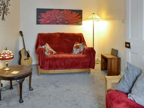 A cozy living room with a red sofa, a wooden coffee table, a guitar, and a lamp.