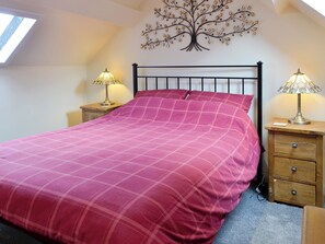 A bedroom with a bed, two nightstands, a wall-mounted tree decoration, and a skylight.