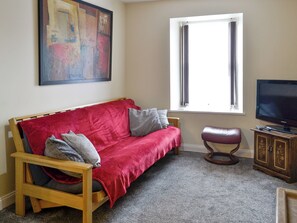 Una sala de estar con un sofá rojo, un mueble de madera, un televisor y una ventana con cortinas.