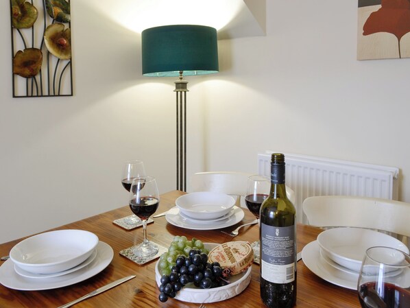 Une table à manger avec des assiettes, des verres, une bouteille de vin et un saladier de raisins.