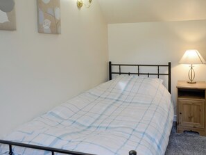 Una cama individual con una colcha a cuadros, una mesita de noche con una lámpara y un aplique de pared.