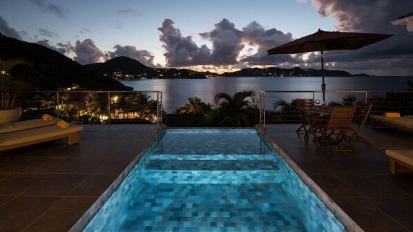 Un espace piscine offrant une vue sur la mer et les montagnes au crépuscule.