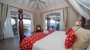 Une chambre spacieuse avec un grand lit, une tête de lit en bois et une vue sur la mer, visible à travers une porte vitrée.