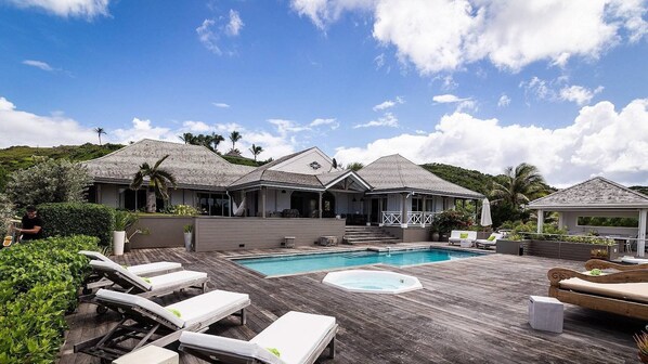 Un espace aménagé au bord de la piscine, avec des chaises longues, un jacuzzi et une terrasse couverte.