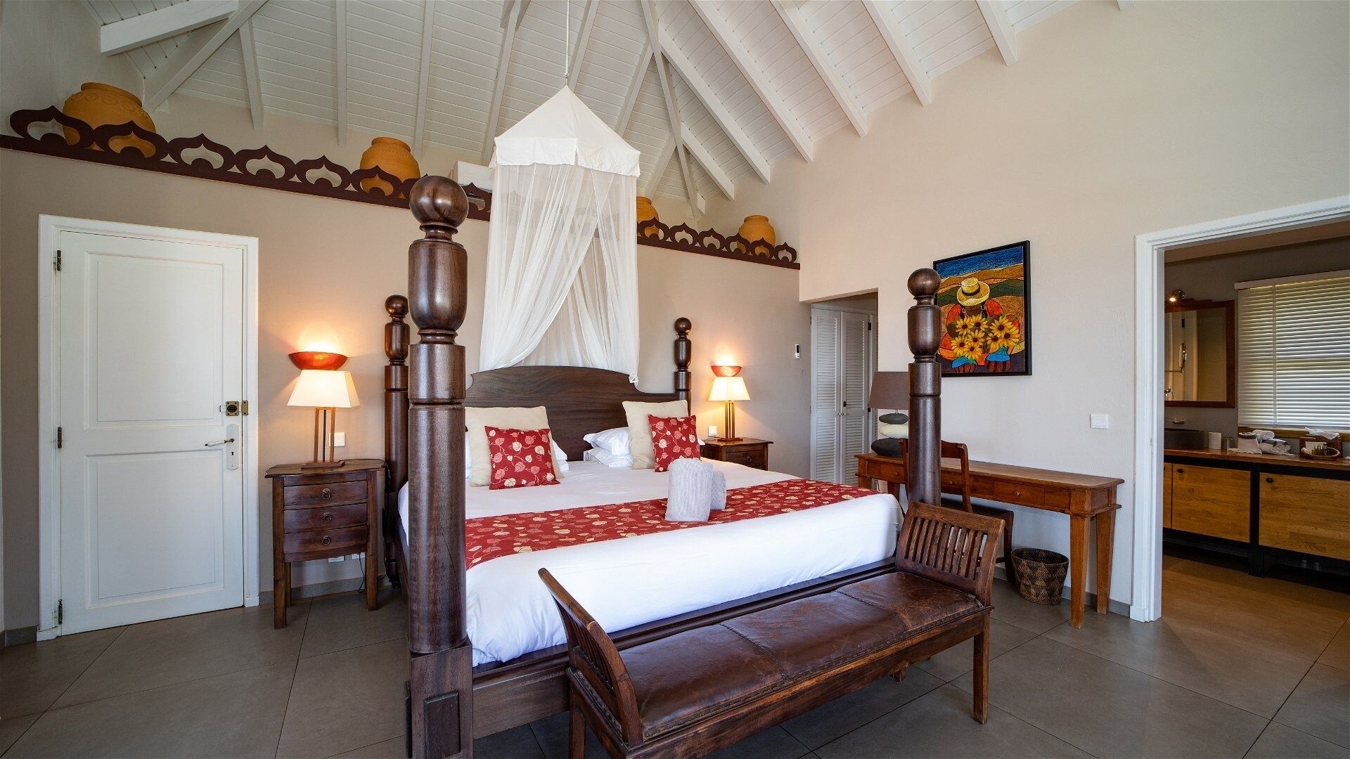 Een ruime slaapkamer met een hemelbed, een houten bankje en een hemel.