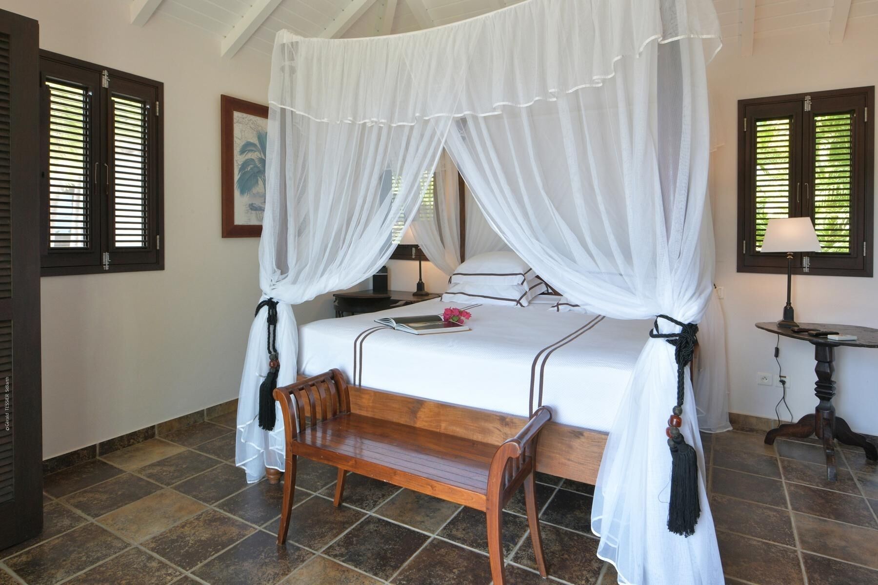 A bedroom with a four-poster bed, a wooden bench, a bedside table, and a nightstand.