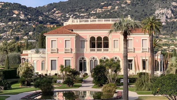 A pink building with arched windows and a balcony, surrounded by a well-maintained garden and a reflective pond. - 04. Bright apartment with balcony and sea view, close to the beach (Saint-Jean-Cap-Ferrat)