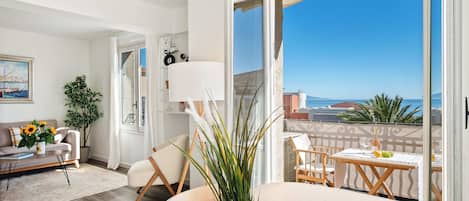 A modern living room with a sofa, a dining table, and a balcony with a view of the sea.