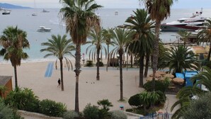 A beach with palm trees, a sandy area, and a view of boats in the water. - 04. Bright apartment with balcony and sea view, close to the beach (Saint-Jean-Cap-Ferrat)