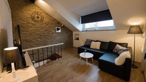 Un dormitorio estilo loft con pared de piedra, un sofá negro, una mesita blanca y una lámpara.