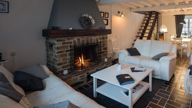 Una sala de estar acogedora con chimenea de piedra, sofás blancos y una escalera que sube a otro nivel.