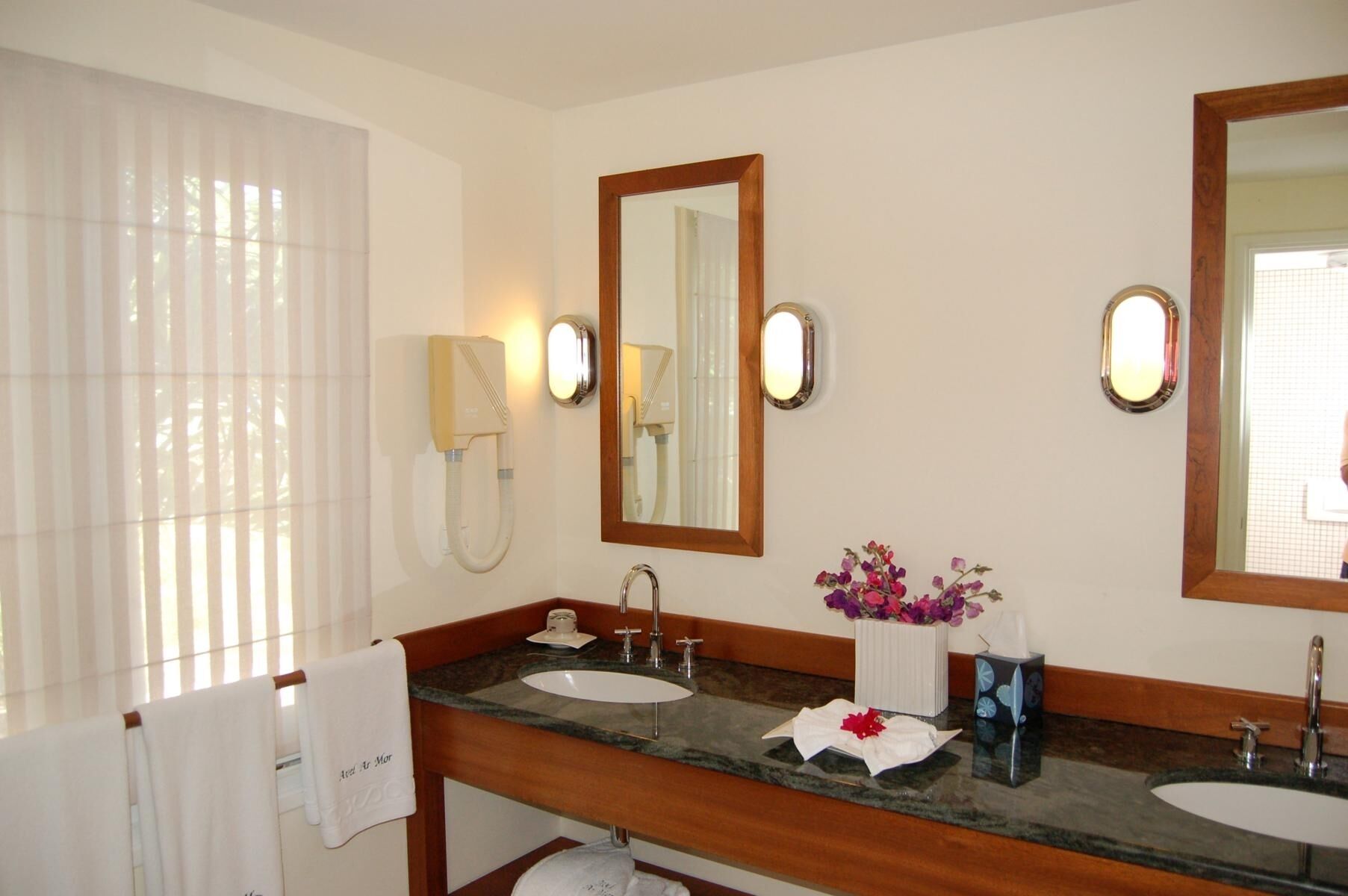 Une salle de bain avec deux lavabos, un miroir, un téléphone et un vase de fleurs.