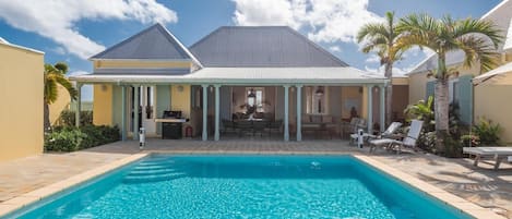 Un espace aménagé au bord de la piscine, avec un patio couvert, des chaises longues et un barbecue.