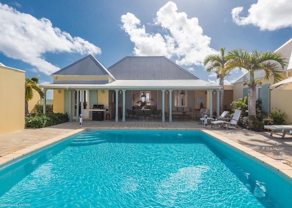 Un espace aménagé au bord de la piscine, avec un patio couvert, des chaises longues et un barbecue.