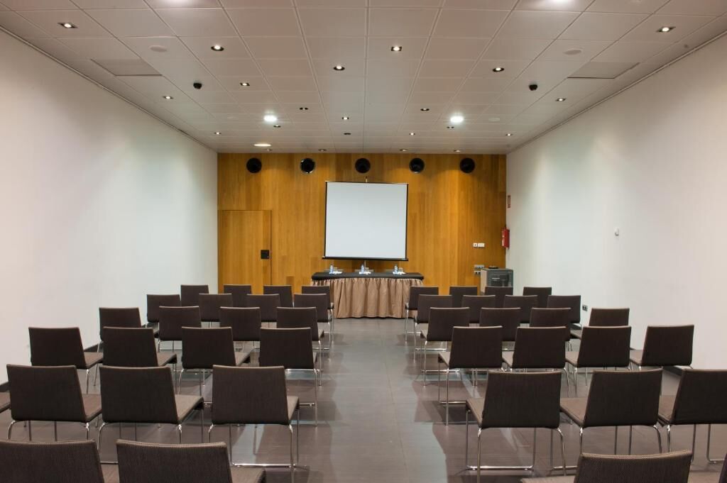 Un salón de conferencias con filas de sillas, un atril y una gran pantalla al frente.