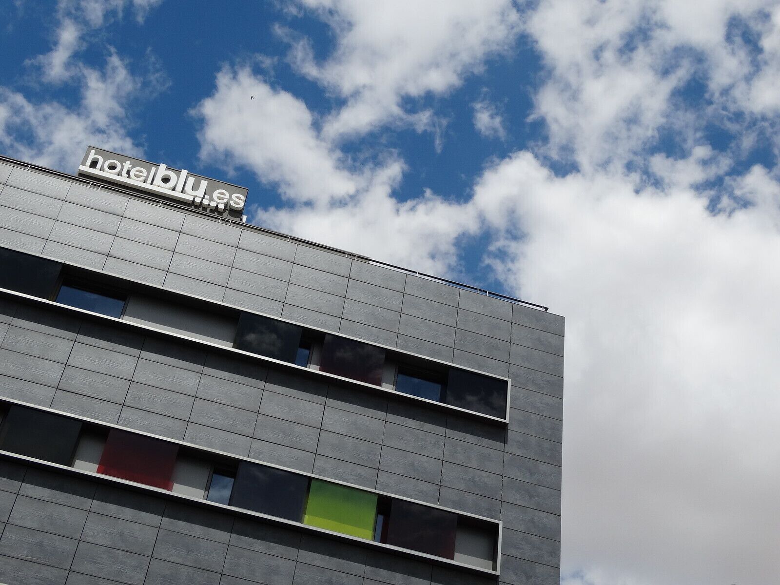 A hotel building with a sign reading "hotelblu.es" against a partly cloudy sky.
