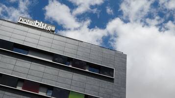Edificio de hotel con un letrero que dice 'hotelblu.es' sobre un cielo parcialmente nublado.