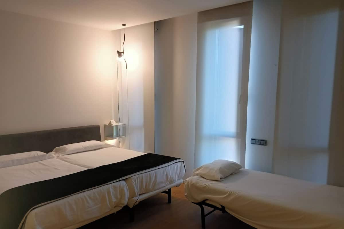 Een slaapkamer met twee bedden, een nachtkastje met een lamp en een raam met gordijnen.