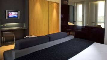 A modern hotel room with a large bed, a desk, a chair, and a TV.
