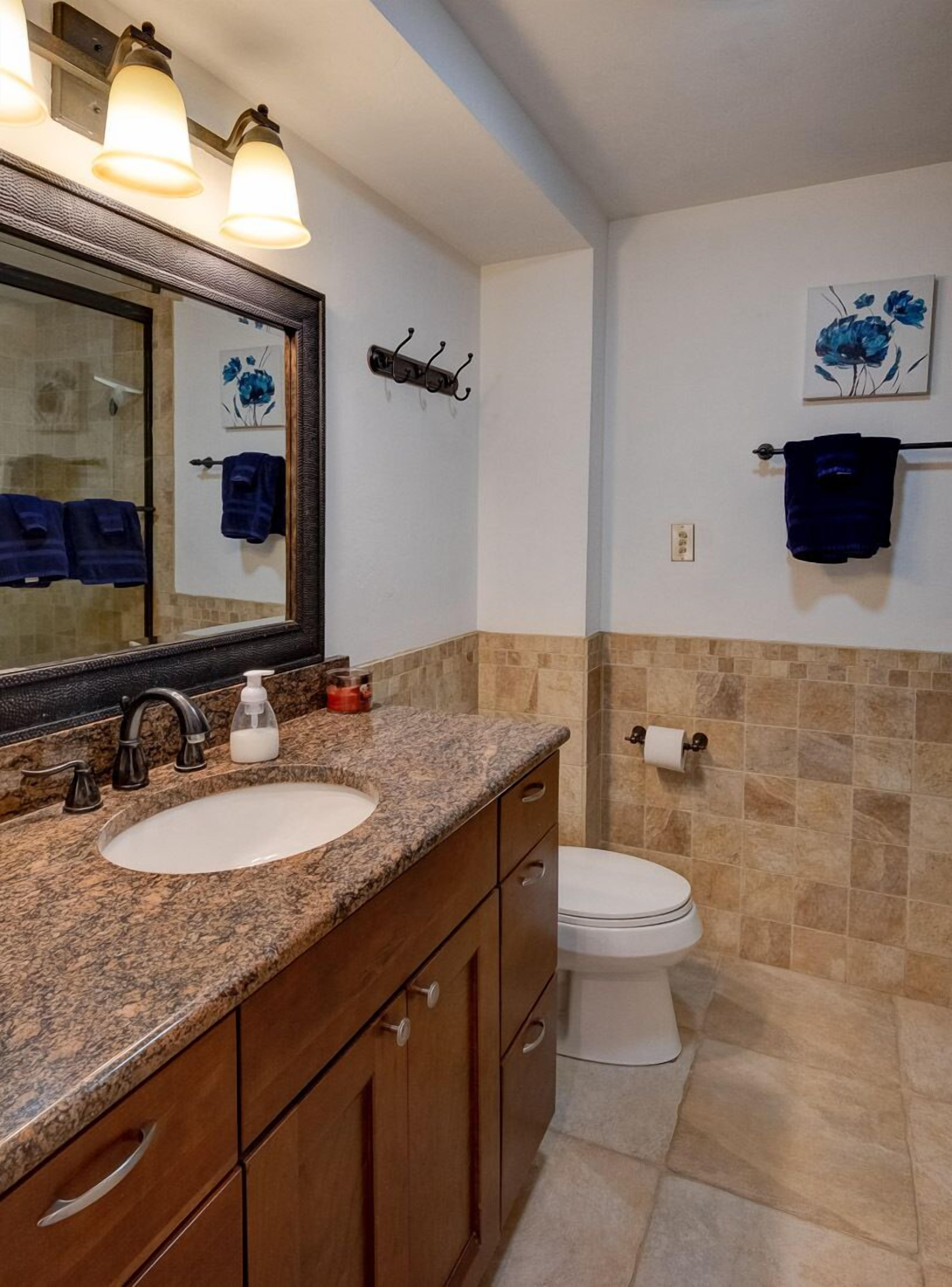 Ein Badezimmer mit Granitplatte, Waschbecken, Spiegel, Toilette und Handtuchhalter.