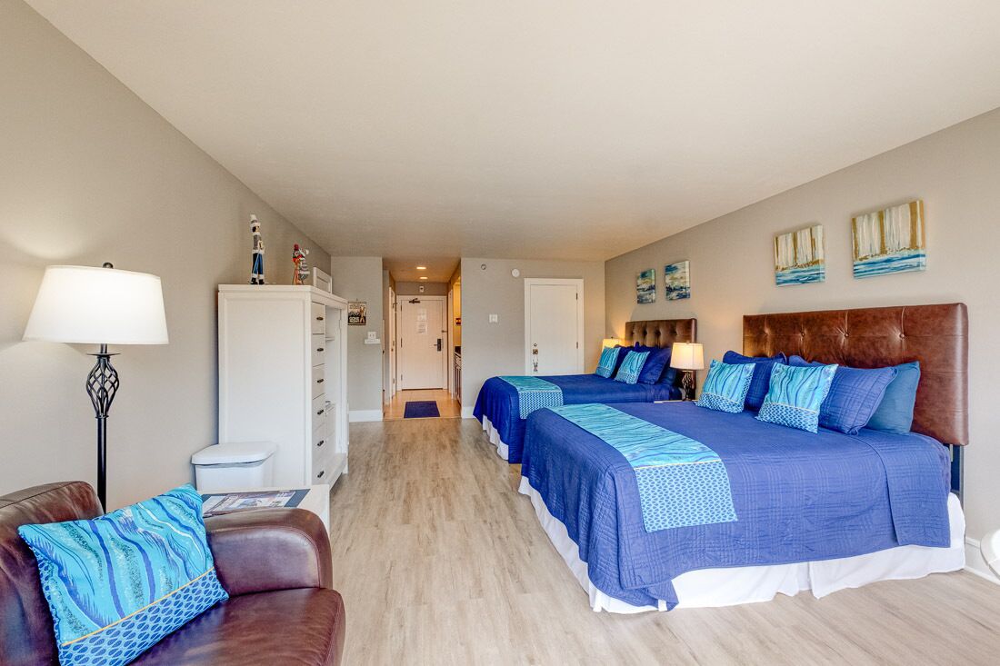Une chambre d’hôtel avec deux lits, un bureau, une chaise, une lampe et une armoire.