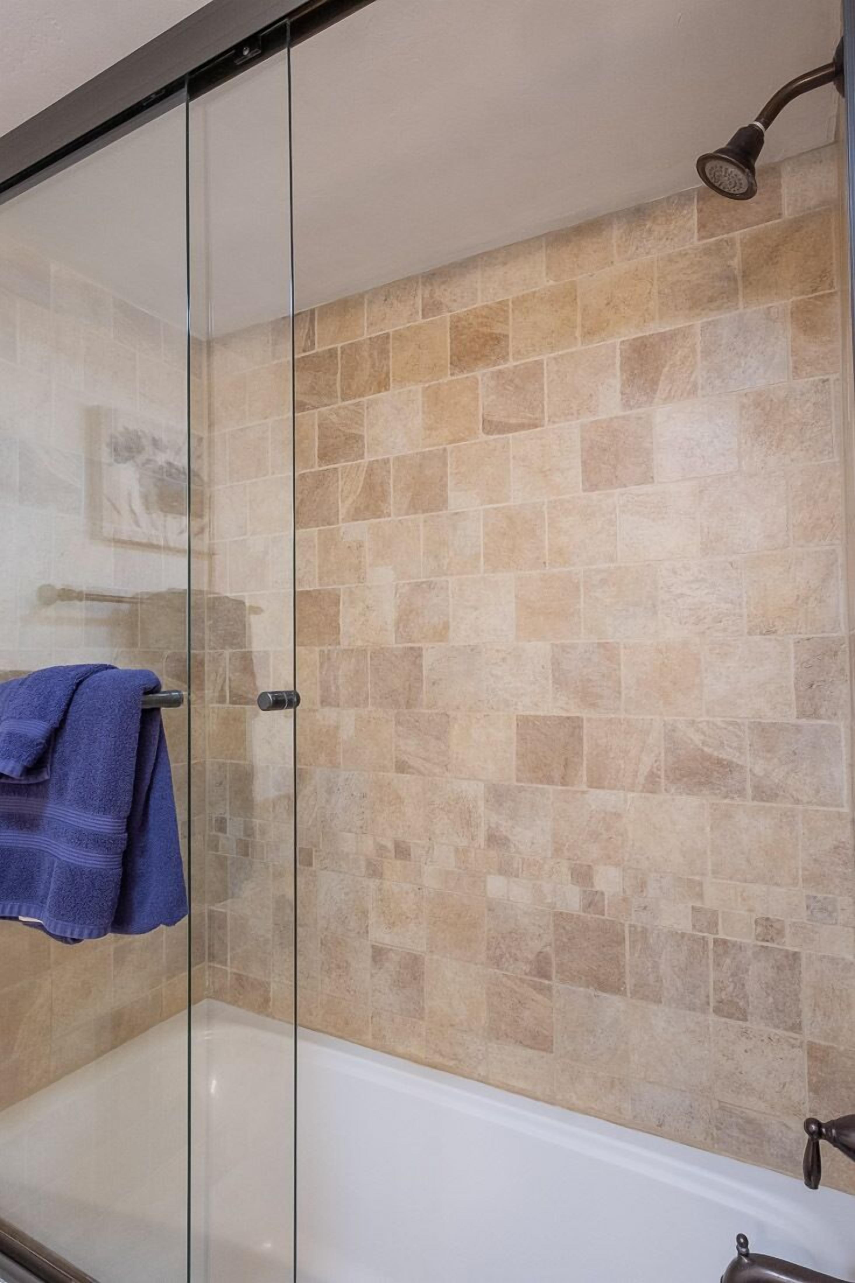 A glass-enclosed shower with beige tiles and a blue towel hanging on the door.