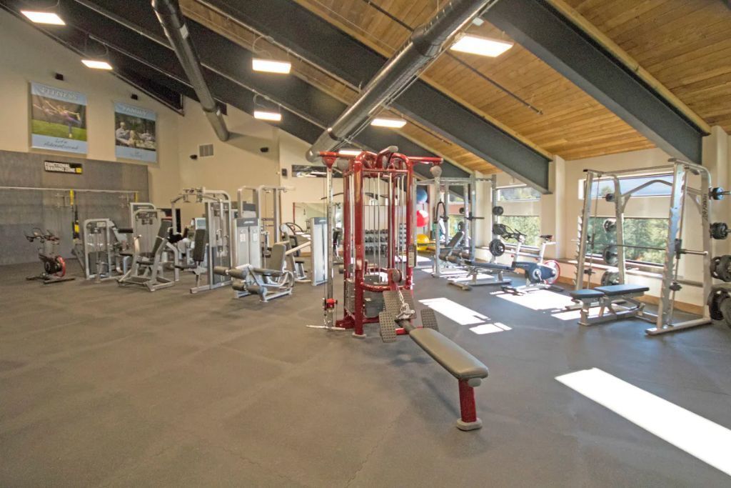 A gym with various exercise equipment, a bench, and a high ceiling with exposed beams.