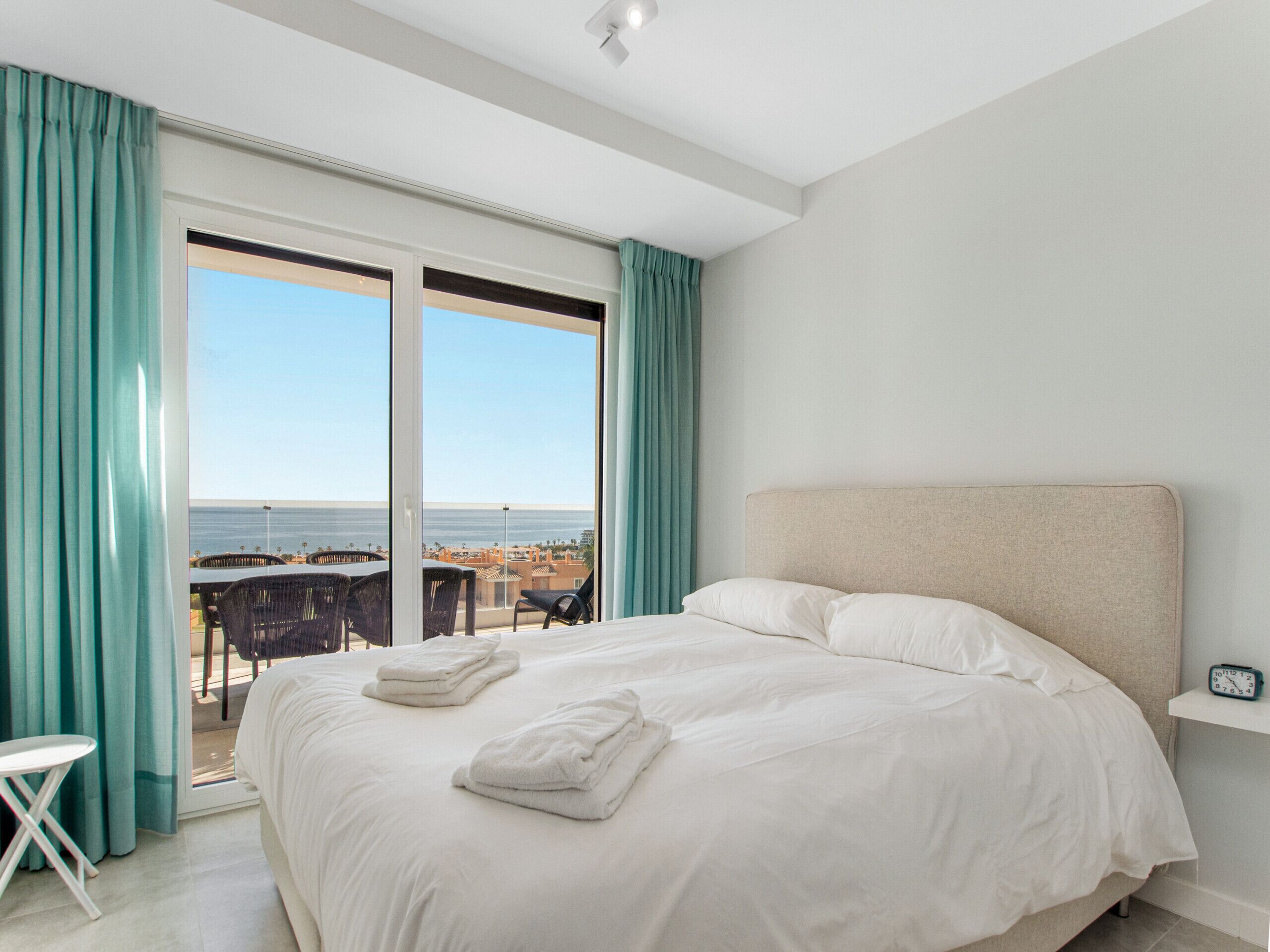 Habitación de hotel con una cama grande, vista al mar y balcón con mobiliario exterior.