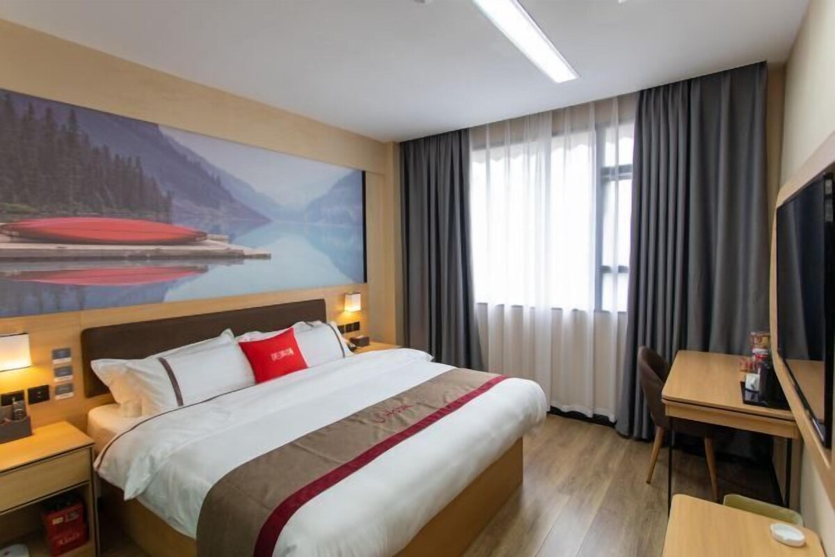 A hotel room with a large bed, a desk, and a painting of a lake.