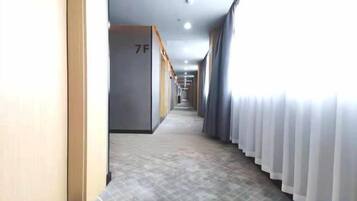 A hotel corridor with doors marked with room numbers, a tiled floor, and a window with curtains.