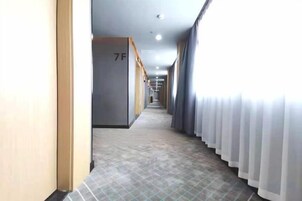 Pasillo de hotel con puertas numeradas, suelo de baldosas y una ventana con cortinas.